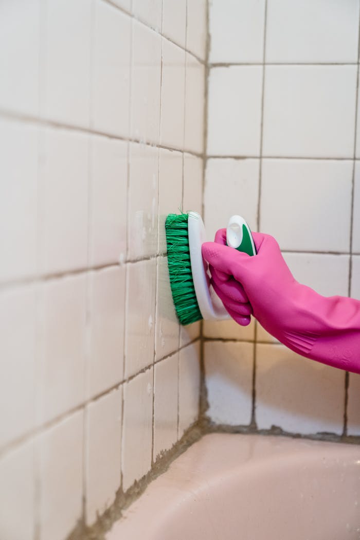 A person scrubs bathroom tiles wearing a pink glove, emphasizing cleanliness.